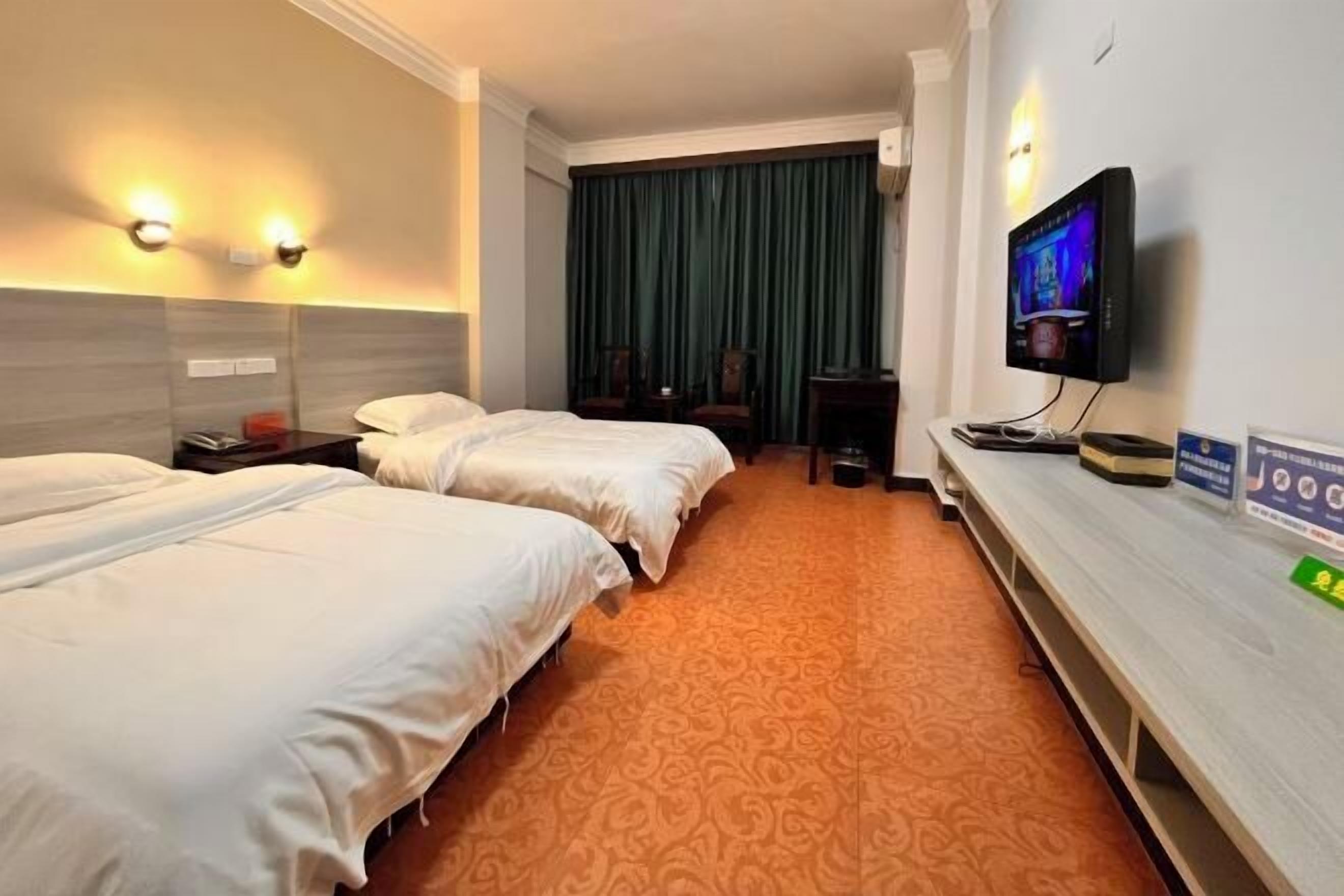 A hotel room with two beds, a TV, a desk, and a large window with curtains.