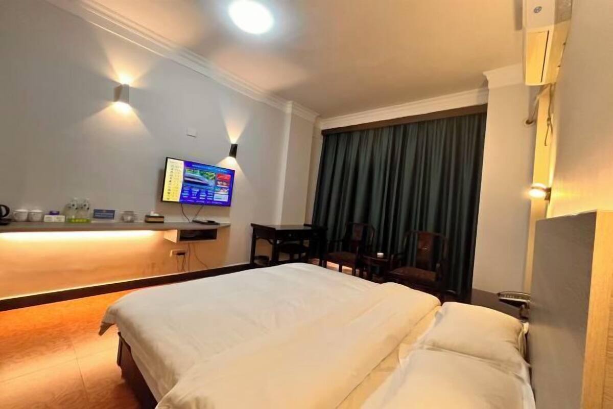 A hotel room with a large bed, a desk with a flat-screen TV, a chair, and a window with curtains.