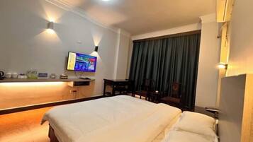 A hotel room with a large bed, a desk with a flat-screen TV, a chair, and a window with curtains.