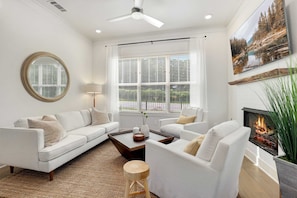 A modern living room with a sofa, armchairs, a coffee table, a fireplace, and a large window with blinds.