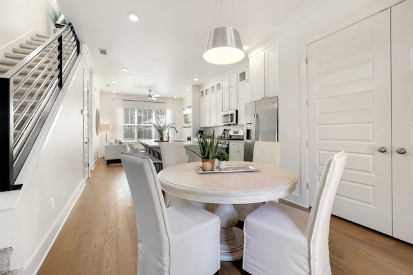 A modern kitchen with white cabinets, a stainless steel refrigerator, and a round dining table with white chairs.
