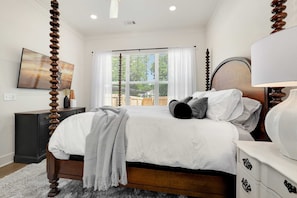 A bedroom with a large bed, a nightstand, a dresser, a lamp, and a window with curtains.