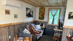 Una sala de estar acogedora con un sofá gris, una mesa de centro de madera y un banco rústico de madera. Se ve una ventana con cortinas estampadas y un cuadro de un zorro.