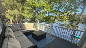 Une terrasse avec un canapé et une table basse, donnant sur un lac où naviguent des bateaux.