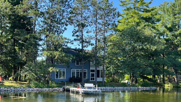 Une maison au bord du lac, avec un quai et un petit bateau.