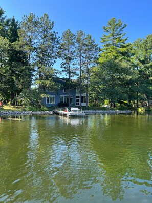 Une maison au bord du lac, avec un quai et un petit bateau.