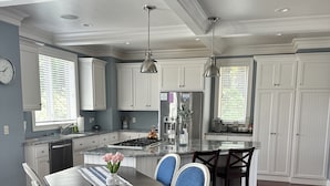 Une cuisine moderne dotée d’un îlot central, de meubles blancs et d’un coin repas avec une table en bois foncé et des chaises recouvertes de tissu bleu.