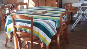 Uma área de refeições com uma mesa e cadeiras de madeira, toalha de mesa listrada, um armário de madeira e um pendente.