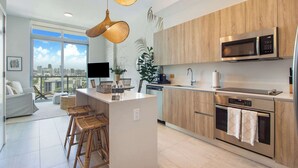 A modern kitchen with a central island, wooden cabinets, a built-in microwave, and a large window offering a city view.