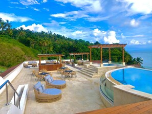 Ein Poolbereich mit Sitzgelegenheiten im Freien, einer Pergola und Blick auf das Meer.