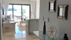 A modern living room with a glass coffee table, white sofas, and a view of the outdoors through large windows. - Beautiful 2 bedroom 3 bed  condominium with big balcony  (Samaná Province)