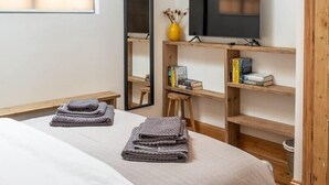 Quarto com cama, televisão em prateleira de madeira, espelho e claraboia.