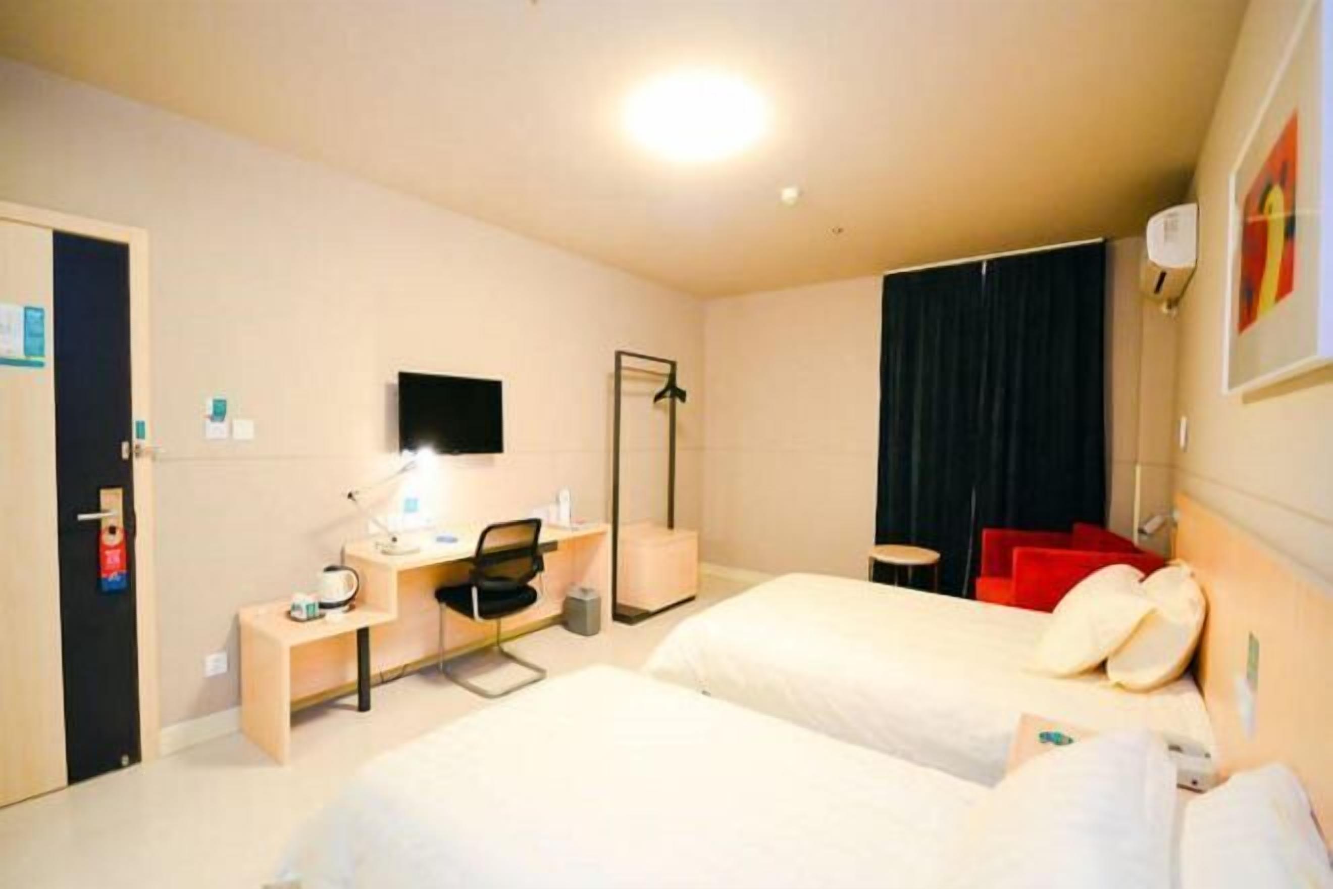 Une chambre d’hôtel avec deux lits, un bureau avec une chaise, un téléviseur à écran plat, un porte-manteau et une petite table.