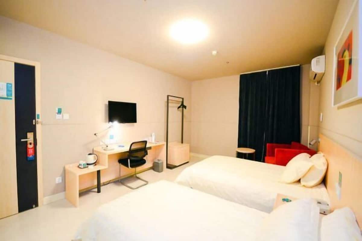 A hotel room with two beds, a desk with a chair, a flat-screen TV, a coat rack, and a small table.