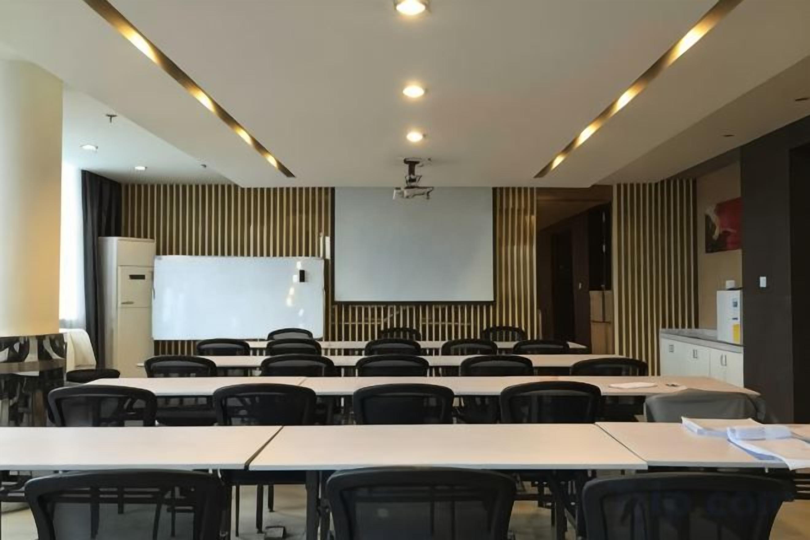 Sala de conferência com quadro branco, projetor e fileiras de mesas e cadeiras.