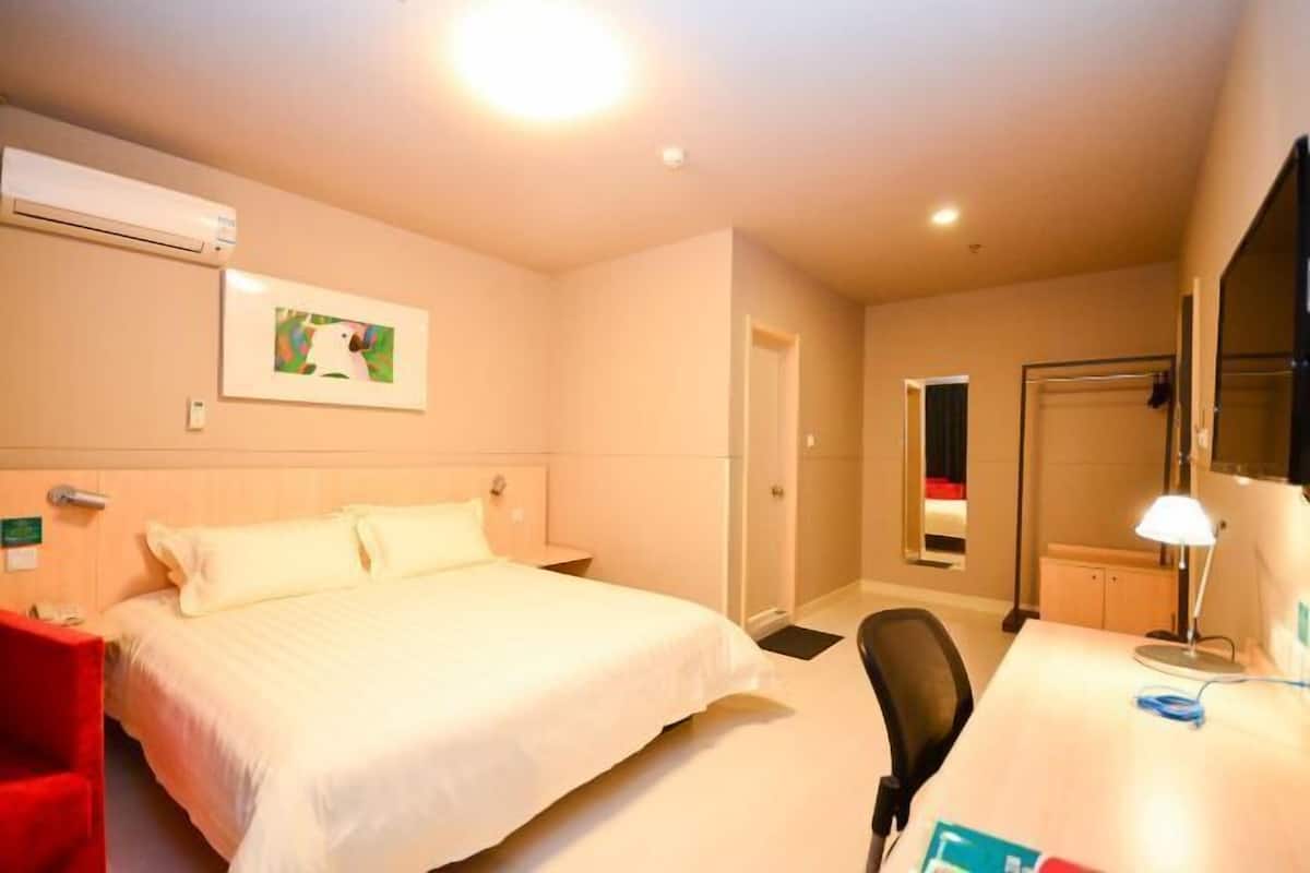 A hotel room with a bed, desk, chair, and an air conditioning unit.
