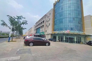 Un hotel con fachada de vidrio moderna, un estacionamiento y una calle con algunos coches.