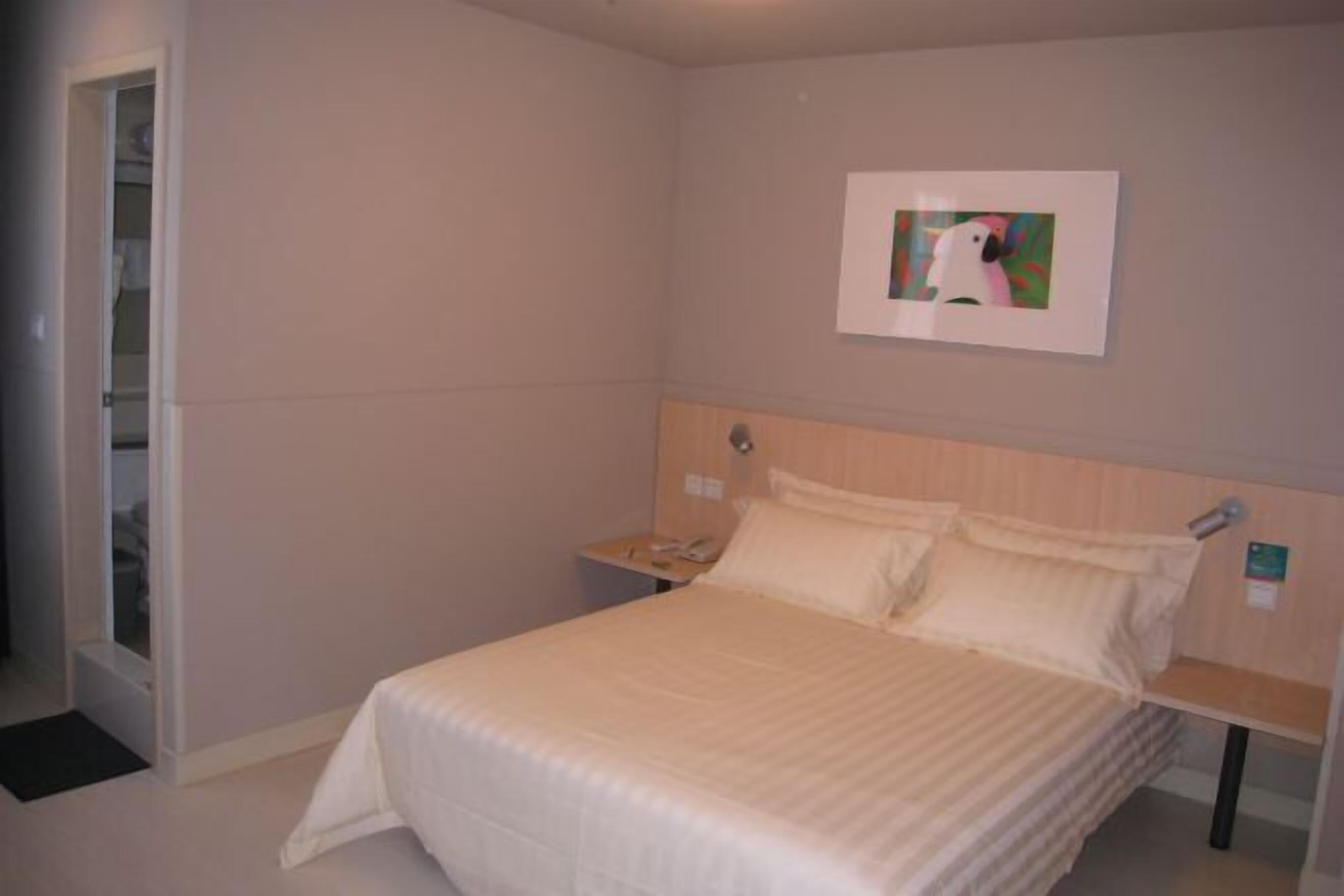 A hotel room with a bed, a nightstand, a wall-mounted phone, and a framed picture.