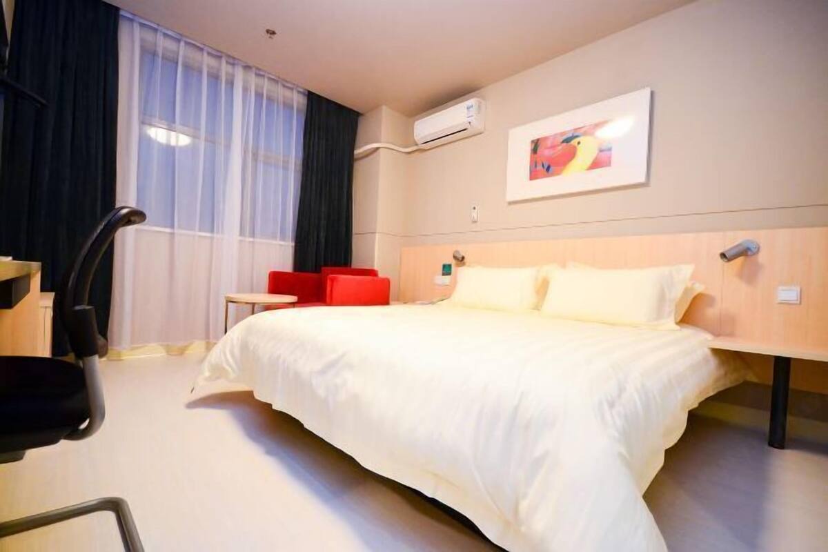 A hotel room with a large bed, a desk, a chair, and a window with curtains.