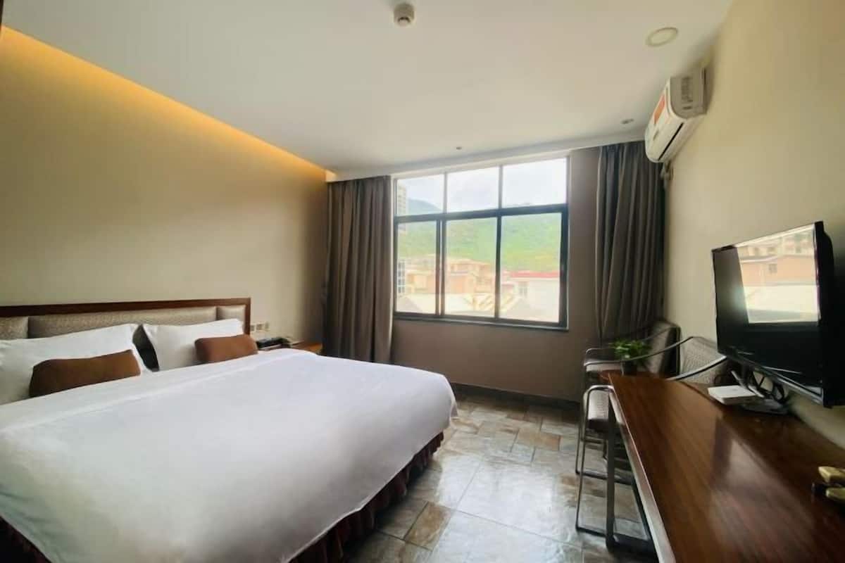 A hotel room with a large bed, a desk with a chair, a television, and a window with curtains.