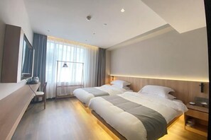 Ett hotellrum med två sängar, ett skrivbord, en stol och ett stort fönster med gardiner.