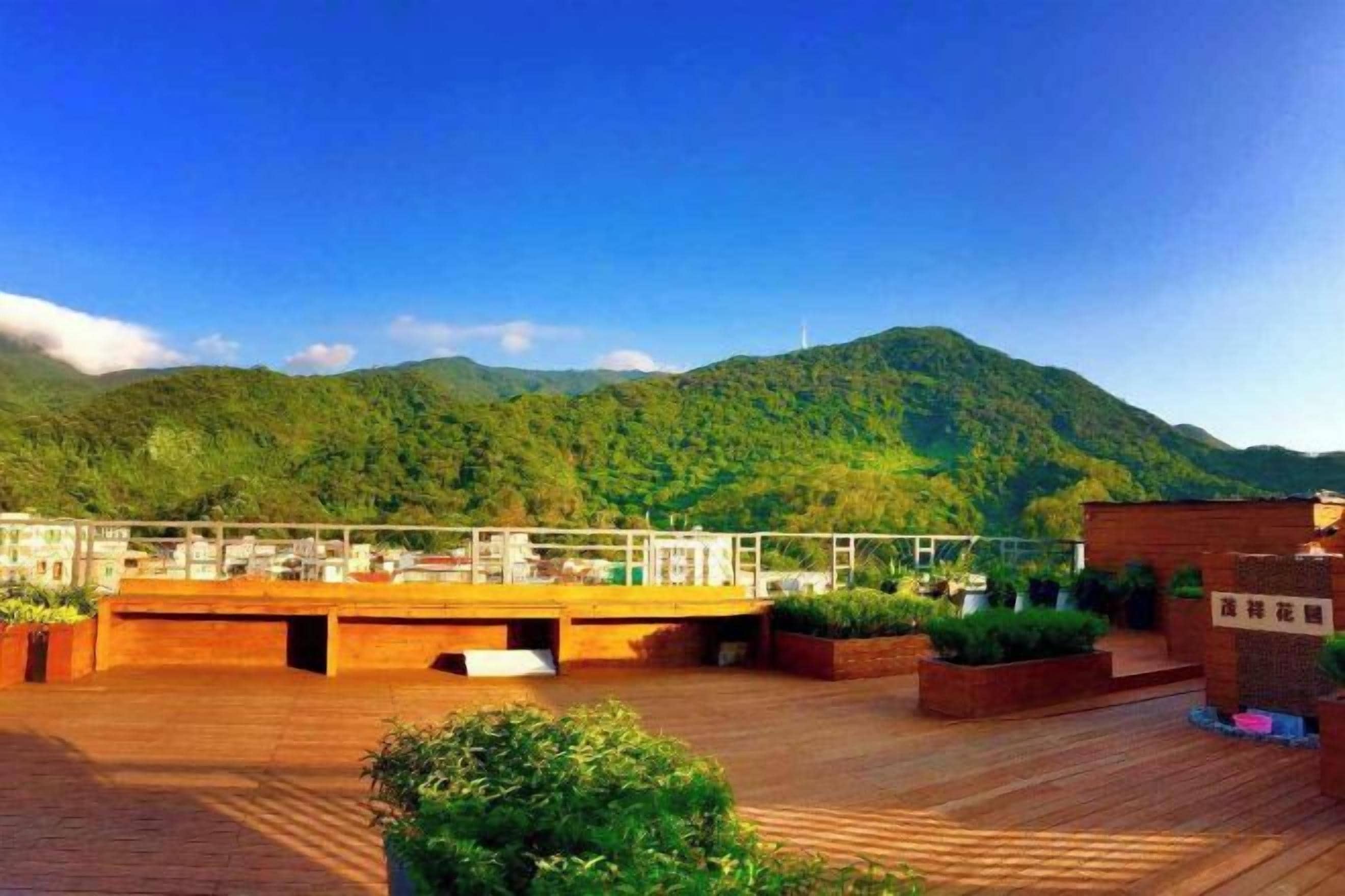 A rooftop terrace with a wooden deck, potted plants, and a view of a mountain range.
