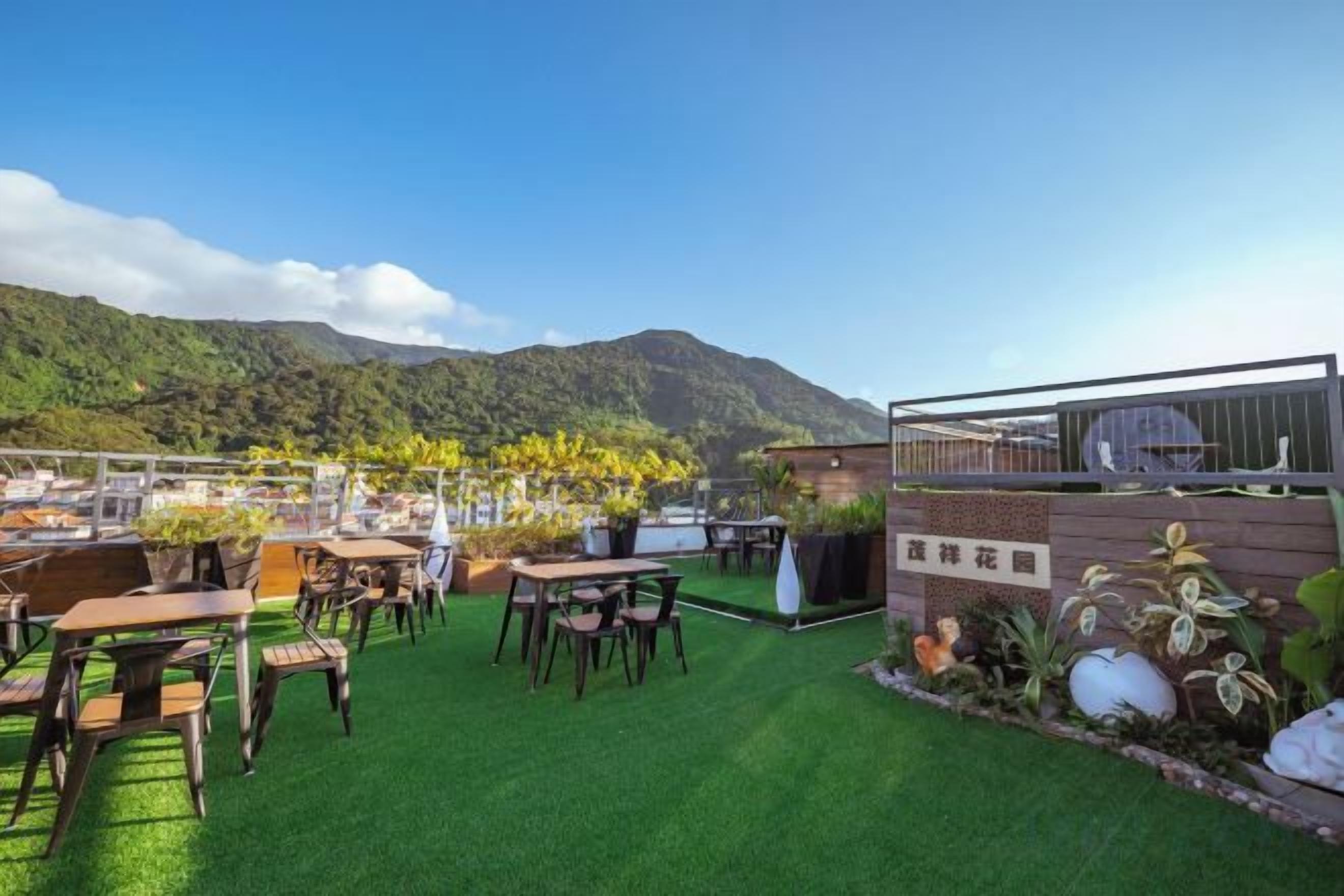 An outdoor seating area with tables and chairs, a green artificial turf, and a view of a mountain.