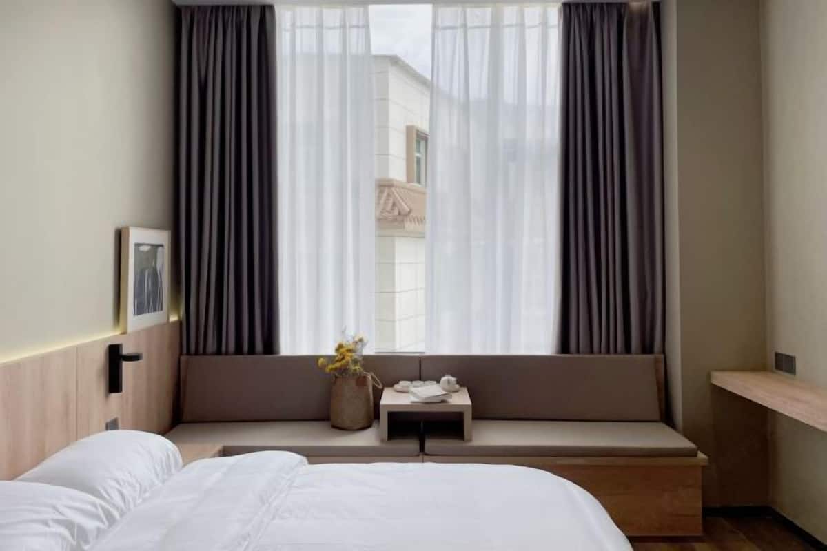 A hotel room with a bed, a small table with a vase of flowers, and a window with curtains.