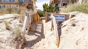 Unes escales de fusta que condueixen a una zona de platja, amb un senyal que diu 'SEA TERN PRIVATE WATER ACCESS'.