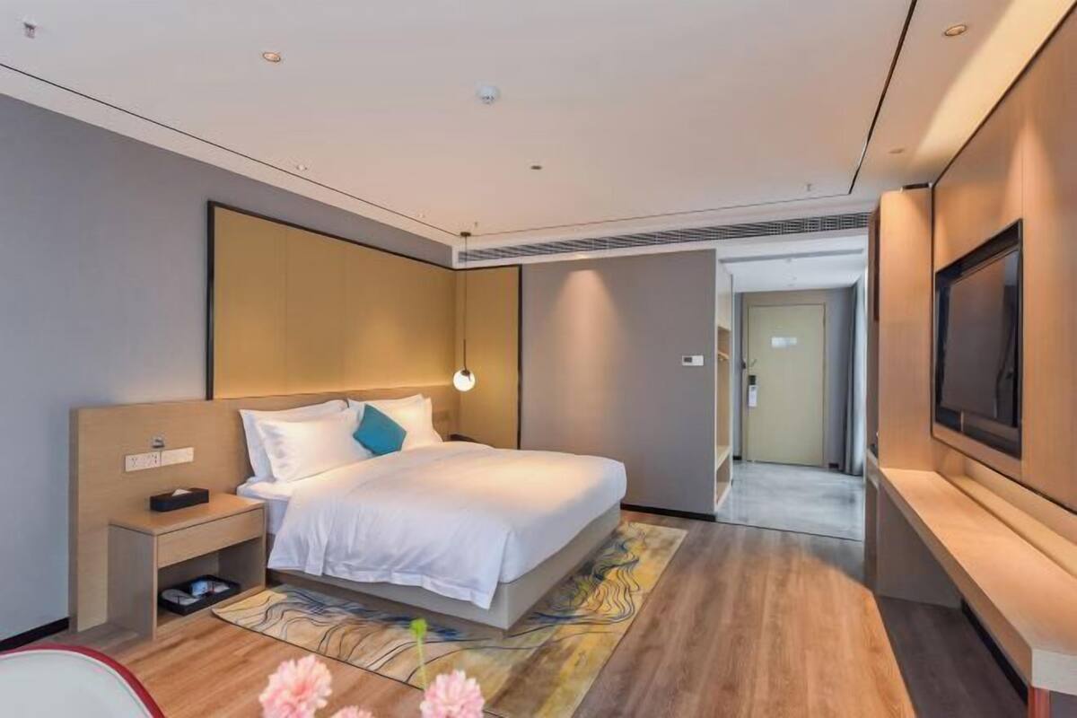Ein modernes Hotelzimmer mit Bett, Nachttisch, Fernseher und Blick auf den Flur.