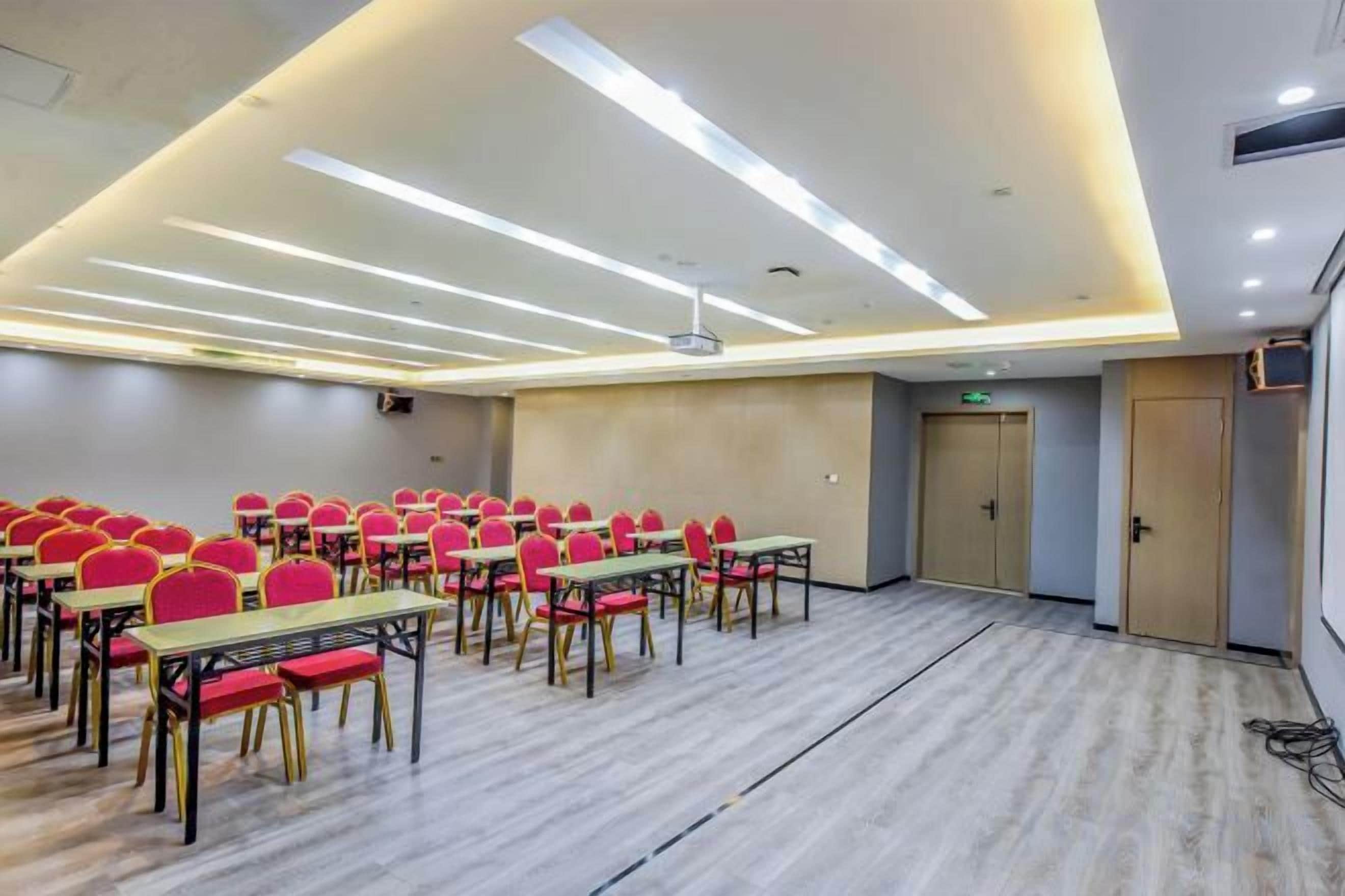 A conference room with rows of tables and chairs, a projector, and a door.