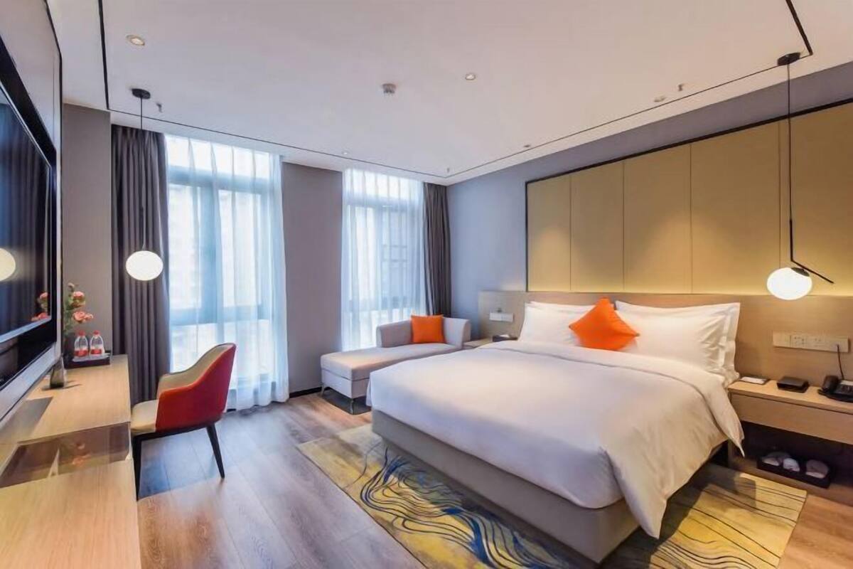 Ein modernes Hotelzimmer mit einem großen Bett, einem Schreibtisch mit Stuhl, einem Fernseher und einem großen Fenster.