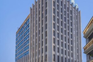 Un edificio alto y moderno con una fachada de ventanas enrejada y un letrero llamativo en la parte superior.