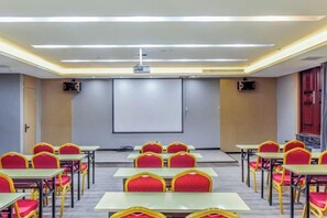 A conference room with rows of tables and chairs, a projector screen, and a presentation screen.