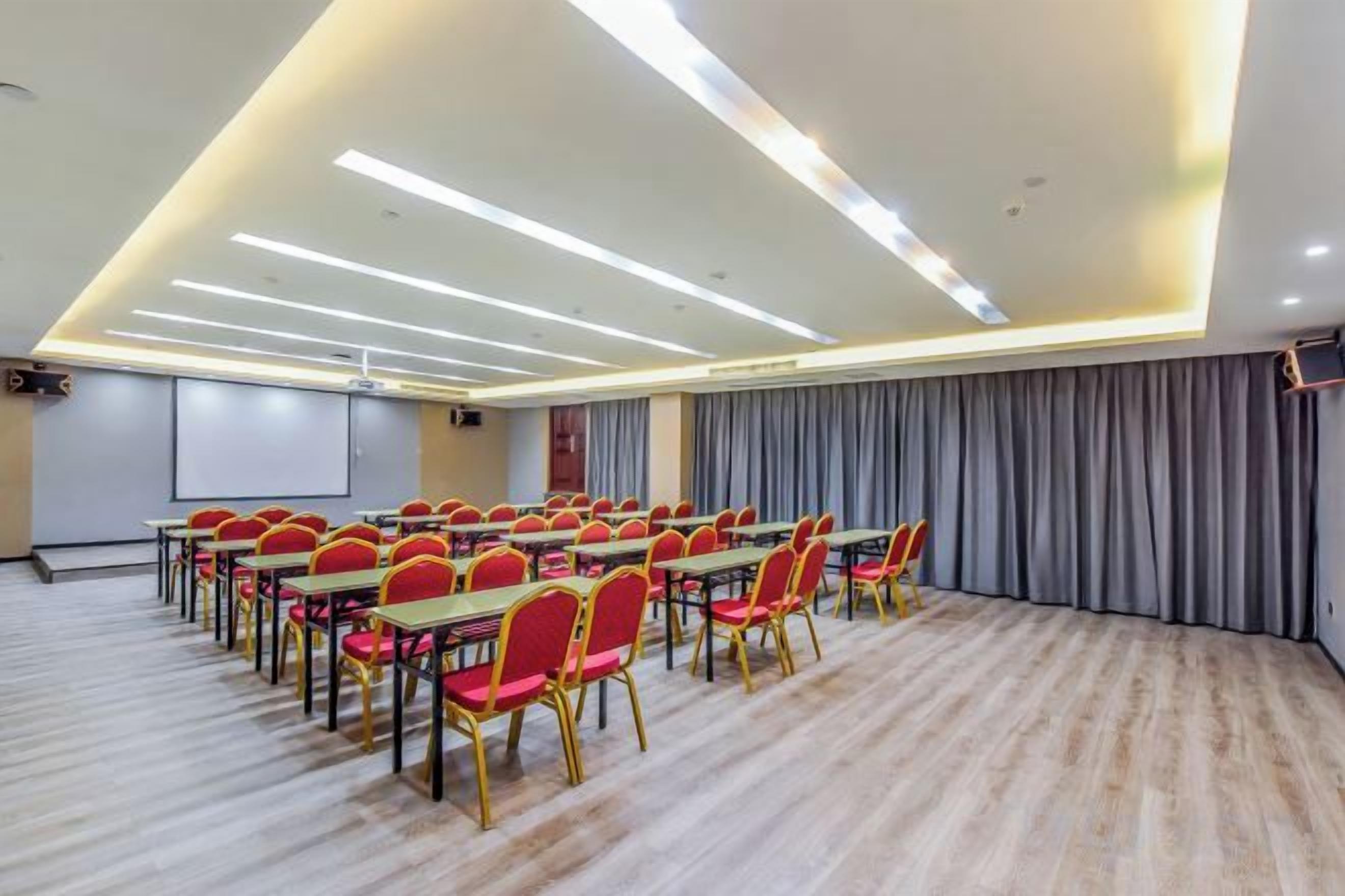 A conference room with rows of tables and chairs, a projector screen, and a large grey curtain.