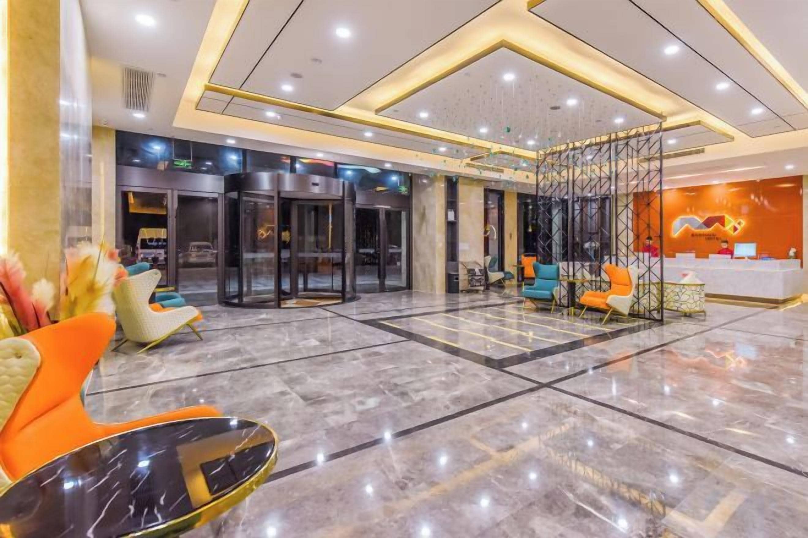 Vestíbulo de hotel con suelo de mármol, una mesa de recepción y una zona de estar con sillas anaranjadas y azules.
