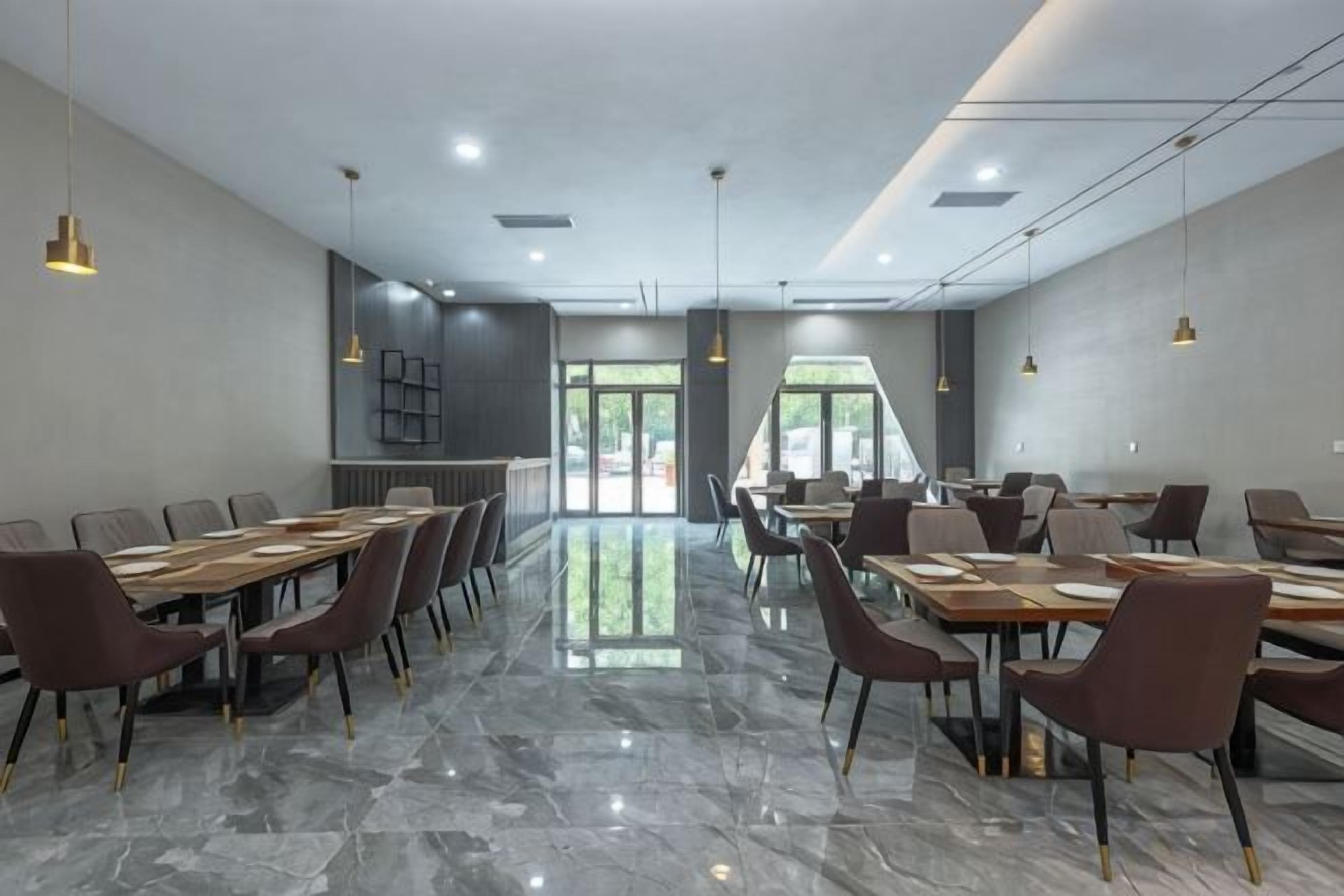 A modern dining area with marble flooring, multiple tables and chairs, pendant lighting, and a view through the glass doors.