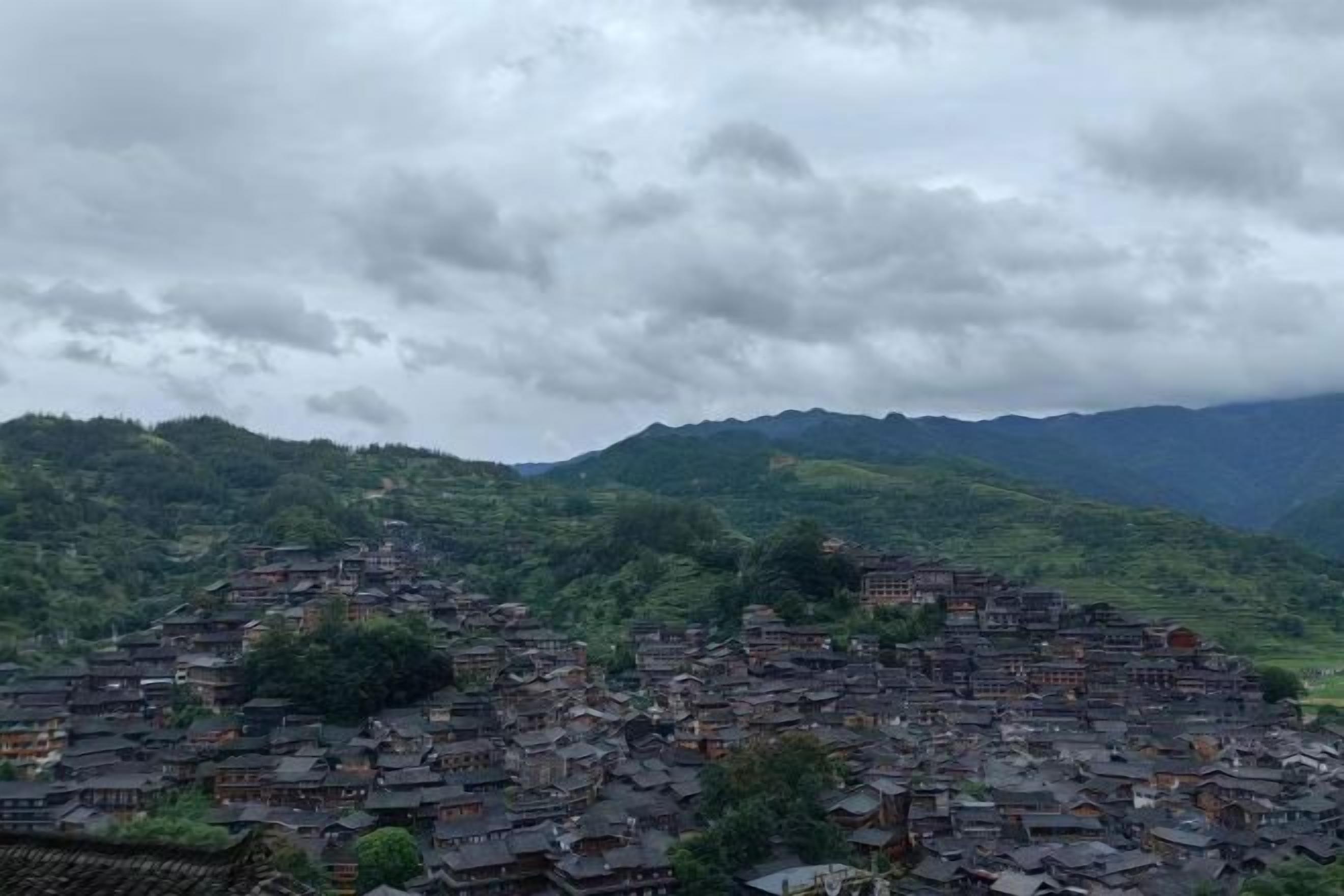 Un pueblo montañoso con edificios tradicionales y una ladera boscosa.