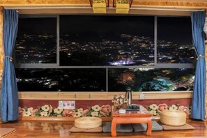 A room with a large window overlooking a cityscape at night, a small table with a vase, and a decorative wall panel. - Xijiang Qianhu Miaozhai Hanshe Inn (Observation Deck Store) (Leishan)