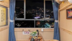 A room with a large window overlooking a cityscape at night, a wooden table with a tray of items, and a framed picture on the wall. - Xijiang Qianhu Miaozhai Hanshe Inn (Observation Deck Store) (Leishan)