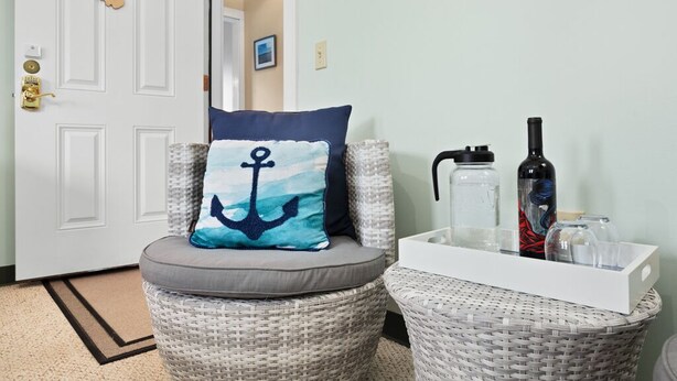 A wicker chair with a cushion featuring an anchor design, a white tray with bottles and glasses, and a door labeled "SAND BEACH SUITE". - Bar Harbor Downtown Suite (Bar Harbor)