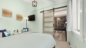 A bedroom with a bed, a TV, artwork, and a sliding door to a bathroom. - Bar Harbor Downtown Suite (Bar Harbor)