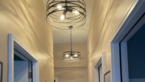 A hallway with a modern chandelier, framed pictures on the walls, and a small table with a lamp. - Bar Harbor Downtown Suite (Bar Harbor)