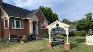 A brick building with a sign for Massage Bar Harbor, listing services like day and medical spa, couples, Swedish, deep tissue, sports, facials, mani & pedi, acupuncture, and medical massage. - Bar Harbor Downtown Suite (Bar Harbor)