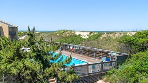 Un espace piscine doté d’une terrasse en bois, entouré de verdure et offrant une vue sur la plage.