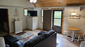 Un salon chaleureux avec un canapé en cuir noir, un téléviseur posé sur un meuble en bois et un coin repas comprenant une petite table et des chaises.
