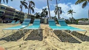 Una playa con tumbonas, palmeras y un edificio con balcones.