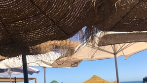 Café al aire libre con mesas y sillas, algunas con sombrillas, con vista al mar.