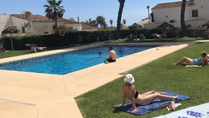 Una piscina con borde de baldosas, rodeada de césped y árboles.