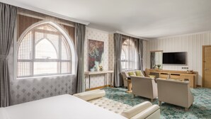 Hotelkamer met een groot bed, twee fauteuils, een bureau en een flatscreen-televisie, plus een groot raam met gordijnen.